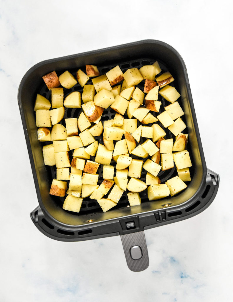 rough cut raw potatoes with oil and seasonings in an air fryer basket before cooking.