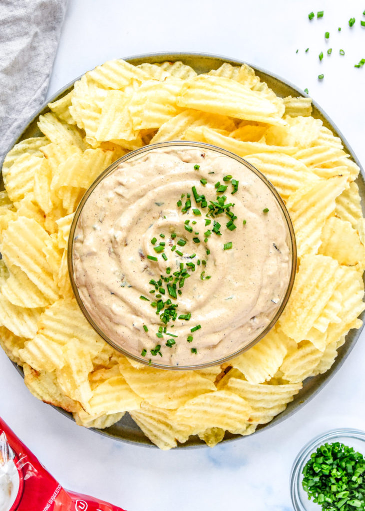 homemade roasted onion dip with chives on top and potato chips on the side.