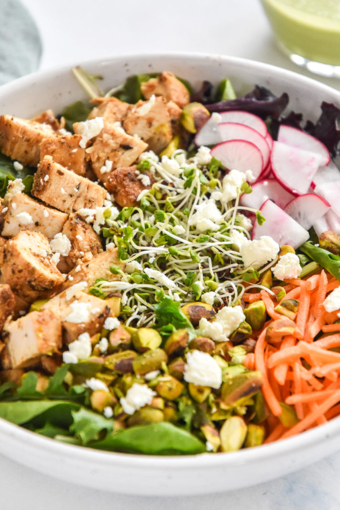 close up photo of simple spring mix lunch salad with chicken, carrots, pistachios, feta cheese, microgreens and more.