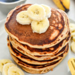 banana protein pancakes stacked on a plate with sliced bananas on top.