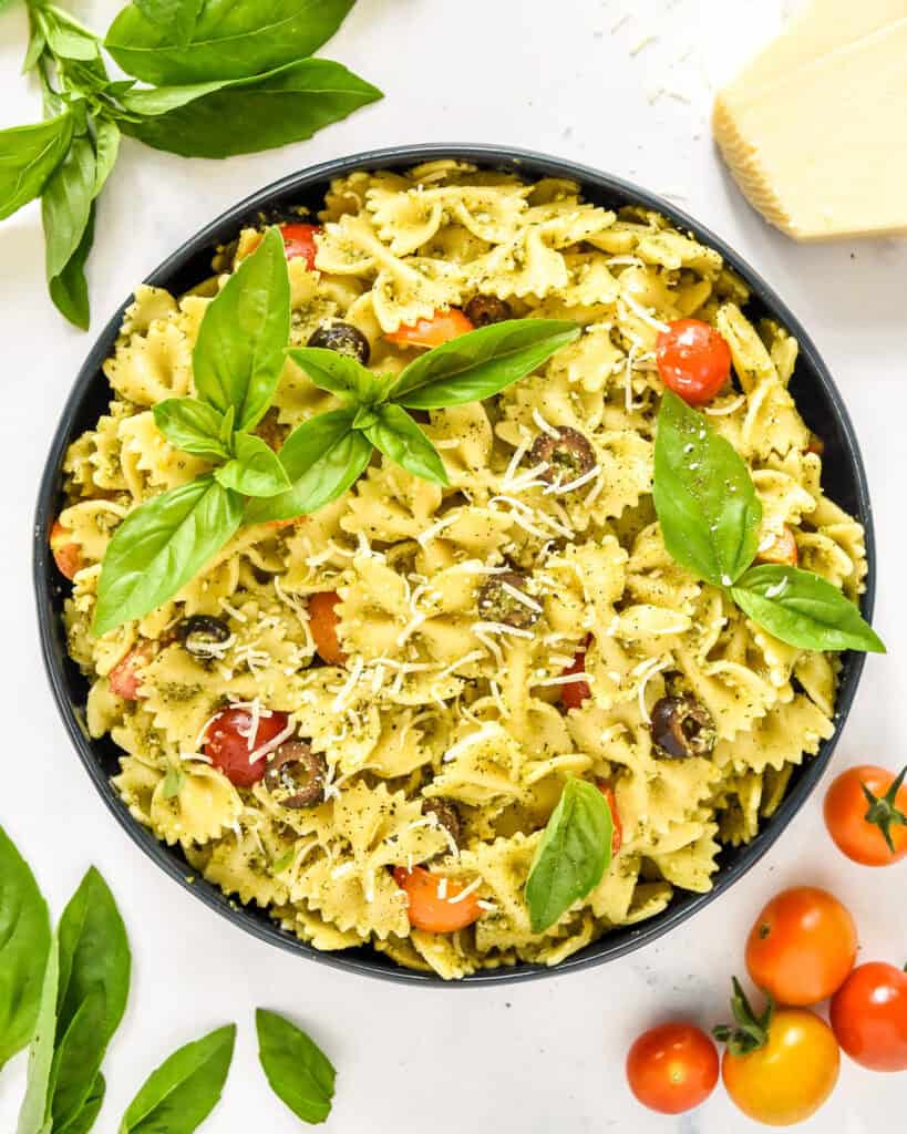 pesto pasta salad in a serving bowl with basil leaves on top.