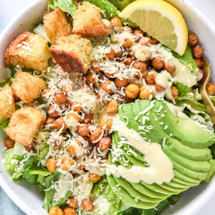 roasted chickpea caesar salad with avocado and croutons in a white bowl.