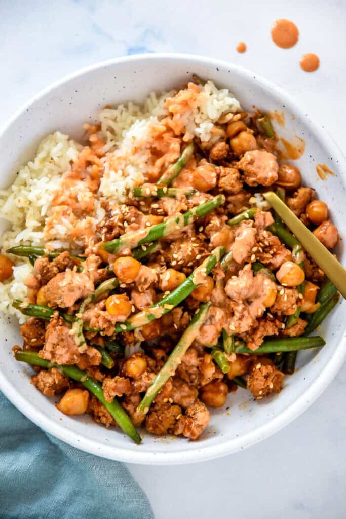 Korean-Inspired Gochujang Meat And Beans in a white bowl with rice, sauce, and a fork.