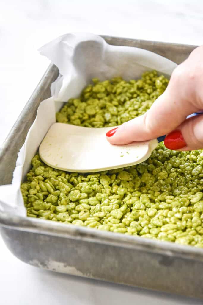 pressing green rice krispies treats into the pan with a silicone spatula.