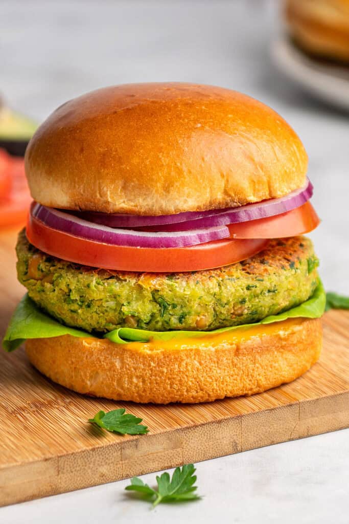 herby chickpea veggie burgers on a bun with tomato lettuce and onion.