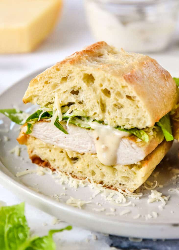 caesar salad chicken sandwiches on a plate cut in half with dressing dripping.