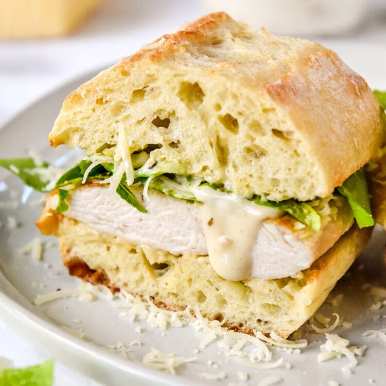 caesar salad chicken sandwiches on a plate cut in half with dressing dripping.