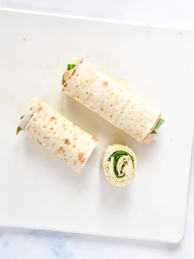 rolled up uncut turkey pesto pinwheel with one sliced off so the inside is visible.