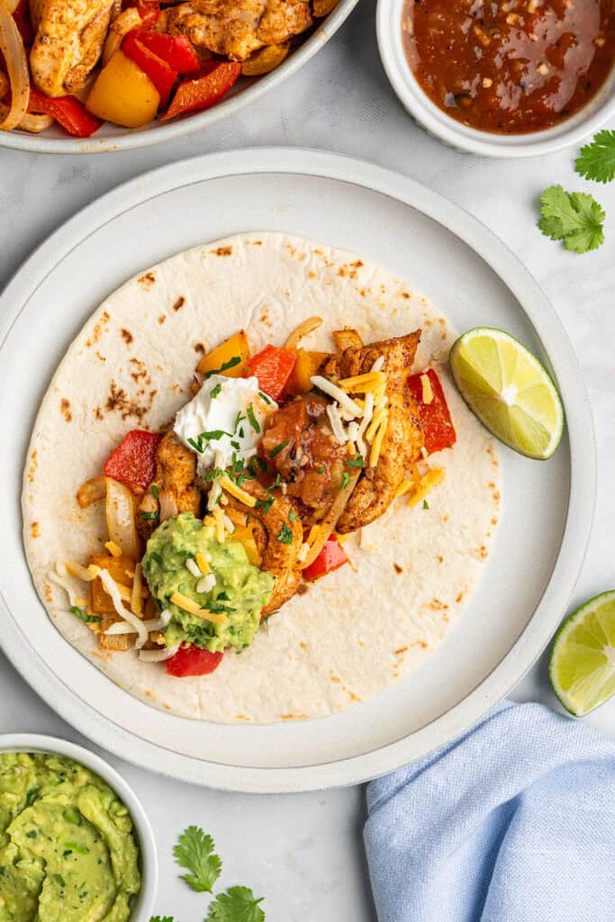 air fryer chicken fajitas plated with shredded cheese, cilantro and avocado.