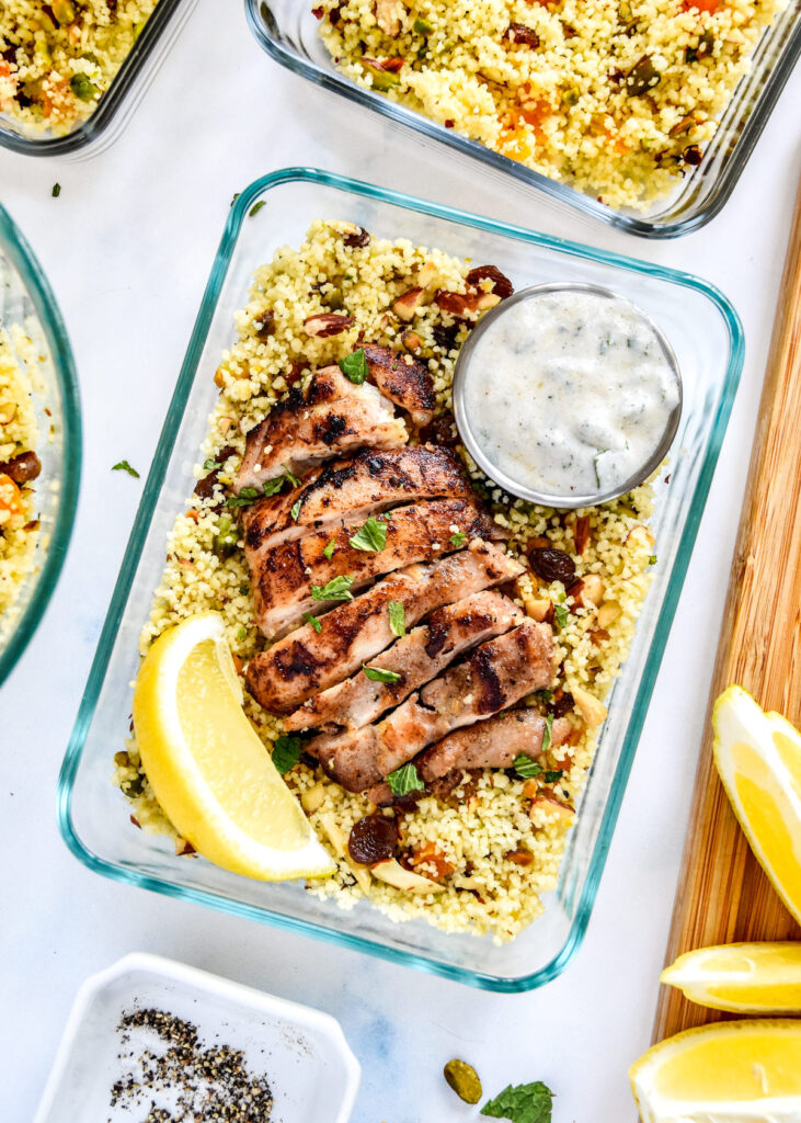 moroccan inspired spiced chicken couscous bowls with yogurt sauce and lemon wedge.