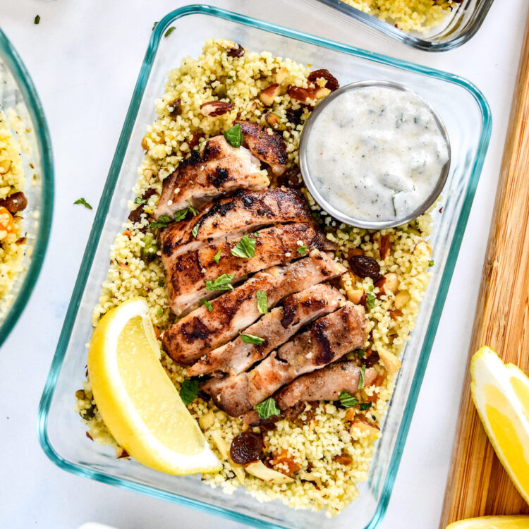 moroccan inspired spiced chicken couscous bowls with yogurt sauce and lemon wedge.