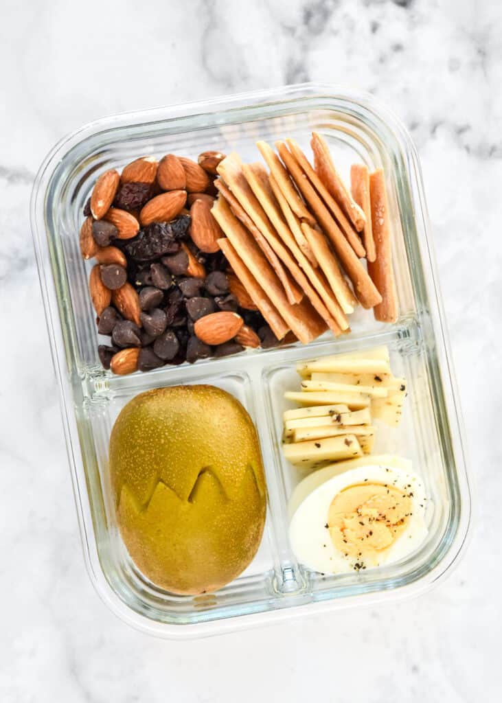 DIY adult lunchable with kiwi, nuts, hard boiled egg, in a glass meal prep container.
