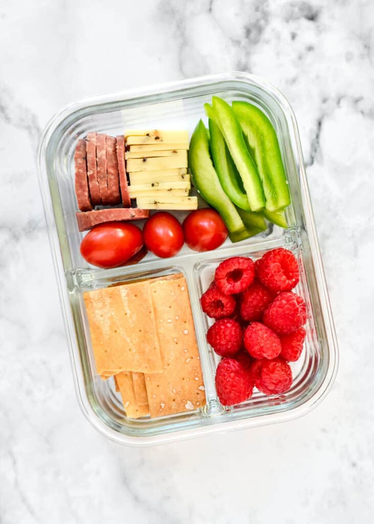 DIY adult lunchable with cheese and crackers in a glass meal prep container.