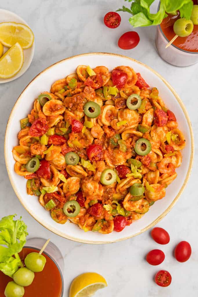 loaded bloody mary pasta salad in a white bowl with green olives on top.
