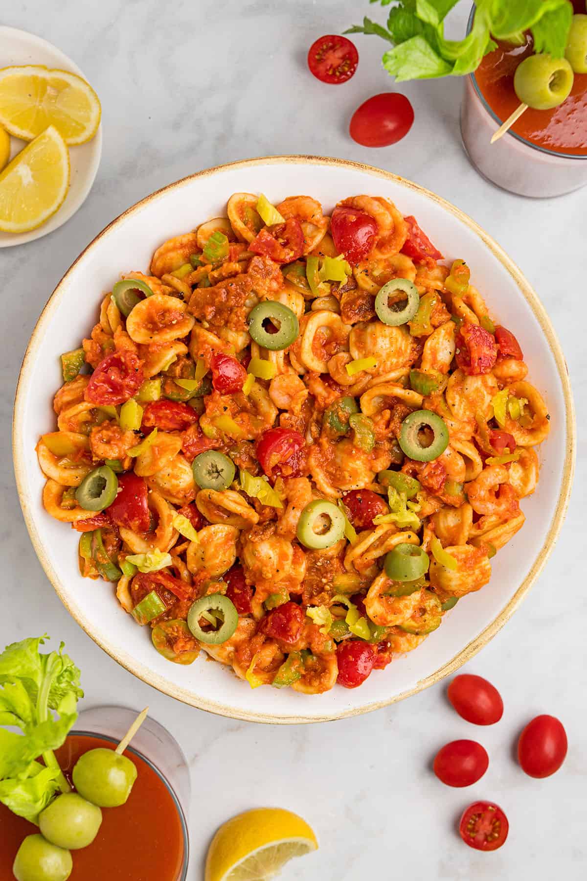 loaded bloody mary pasta salad in a white bowl with green olives on top.