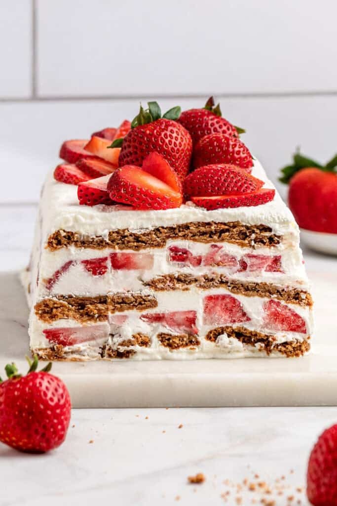 strawberry gingersnap icebox cake with fresh strawberries on top, sliced to see the interior.