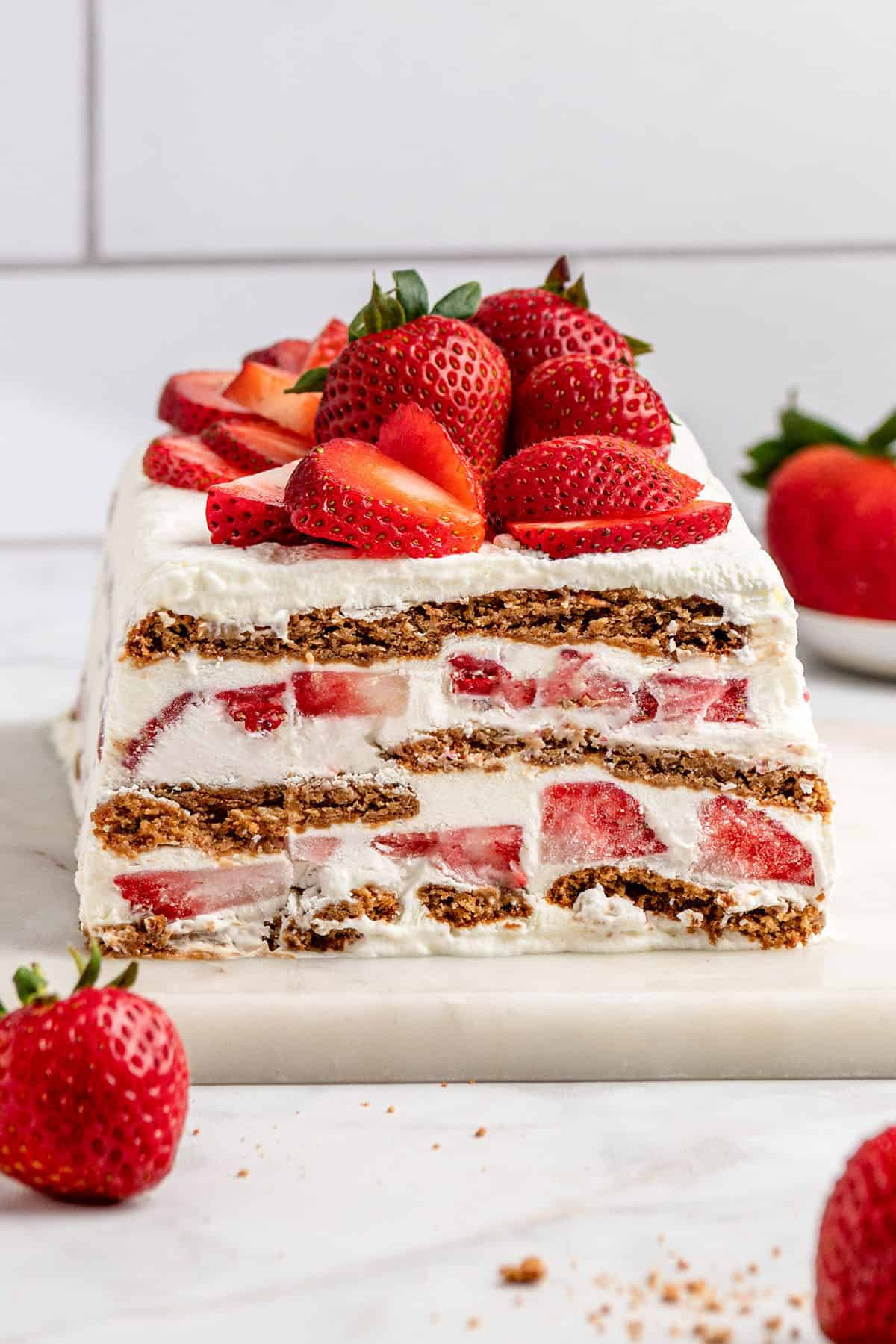 strawberry gingersnap icebox cake with fresh strawberries on top, sliced to see the interior.