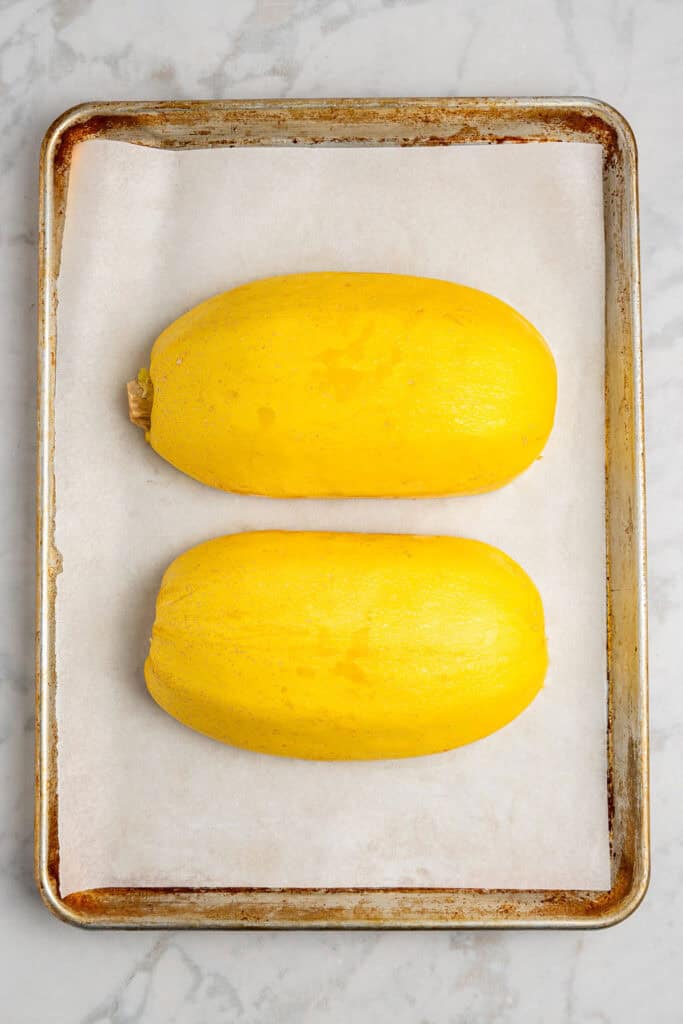spaghetti squash cut in half and placed cut side down on a lined sheet pan.