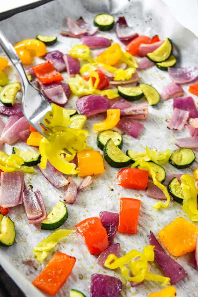 adding pepperoncinis to a sheet pan of vegetables.