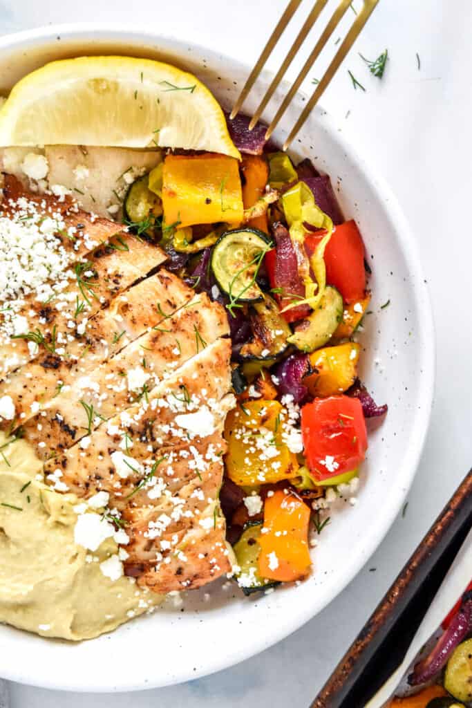Easy Oven Roasted Summer Vegetables in a bowl with chicken and hummus.