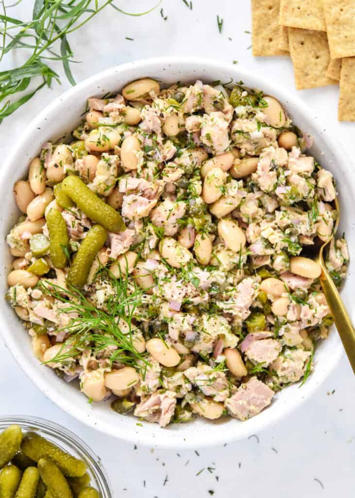 French-Style Tuna White Bean Salad in a bowl with fresh herbs, gherkins and a spoon in the bowl.
