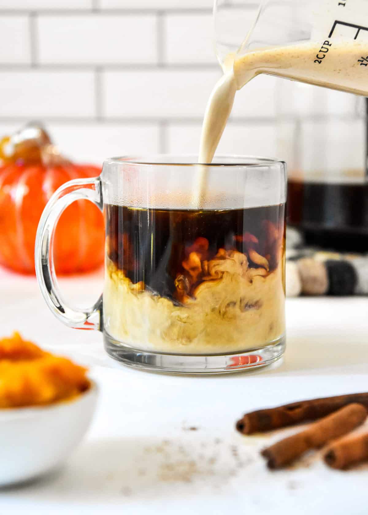 pouring homemade pumpkin spice coffee creamer into a cup of black coffee.