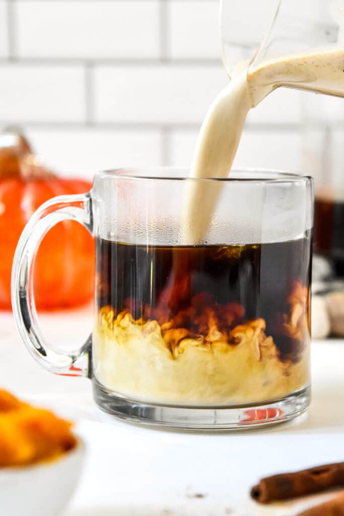 pouring homemade pumpkin spice coffee creamer into a cup of coffee.