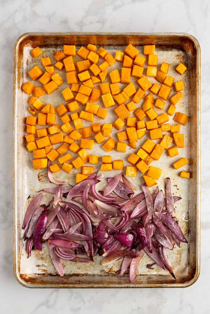 cooked diced squash and red onion wedges on a rimmed sheet pan.
